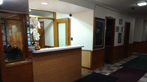 A reception area with a wooden reception desk, a check-in counter, a small white flower arrangement, and a check-in counter with a sign.