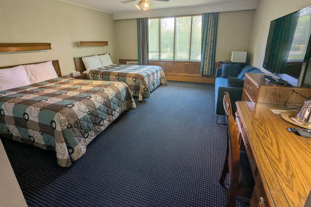Ein Hotelzimmer mit zwei Betten, einem Schreibtisch, einem Fernseher und einem Deckenventilator.