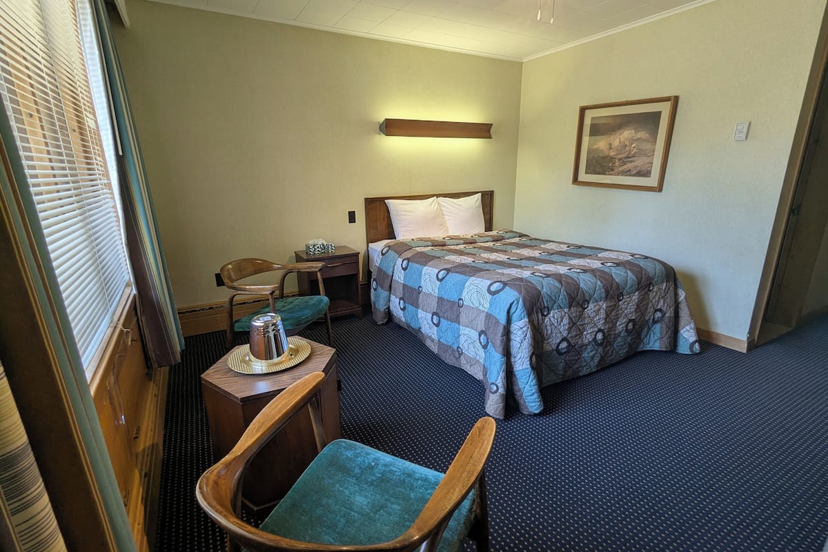 Ein Hotelzimmer mit einem Bett, einem Sessel, einem kleinen Tisch mit einer Tasse, einem Nachttisch und einem Bild an der Wand.