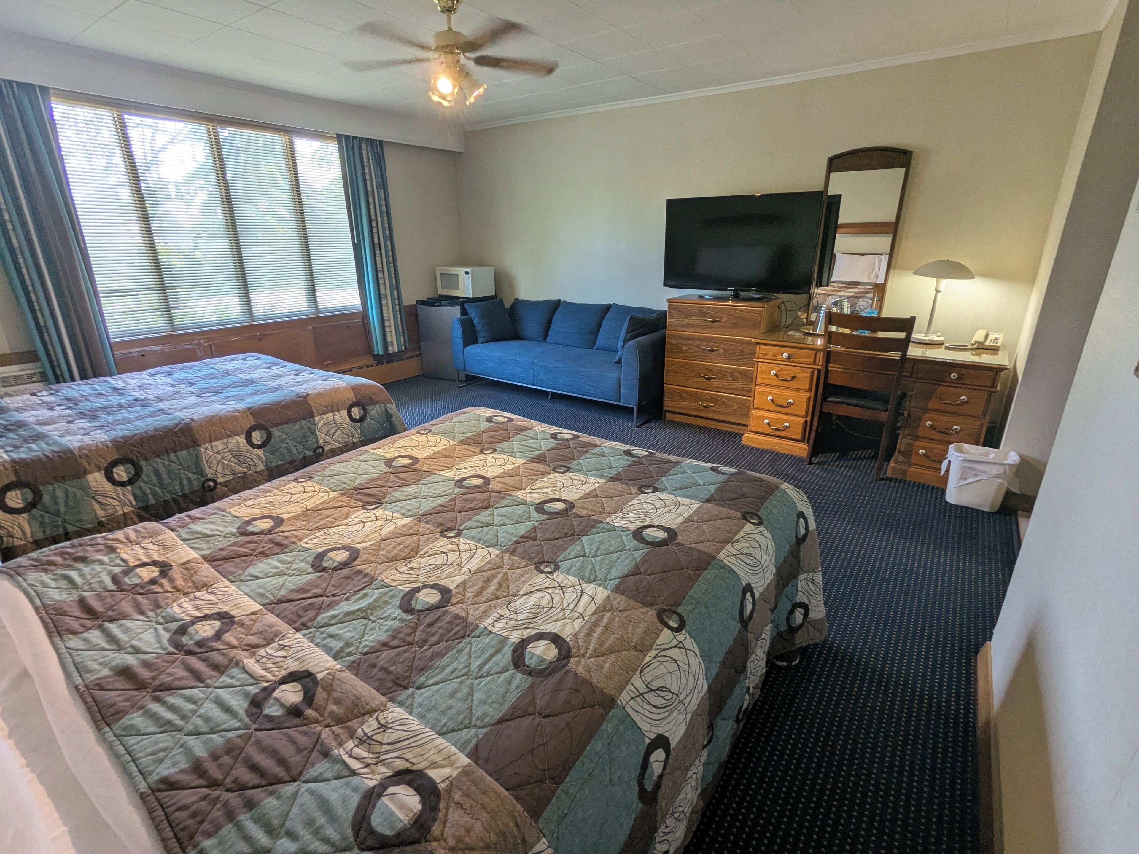 A hotel room with two beds, a TV, a dresser, and a ceiling fan.