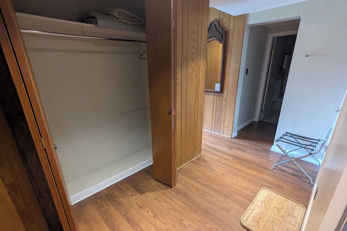 Ein Zimmer mit Holzboden, einem Schrank mit Holztür, einem Metalldörr und einer kleinen Fußmatte.