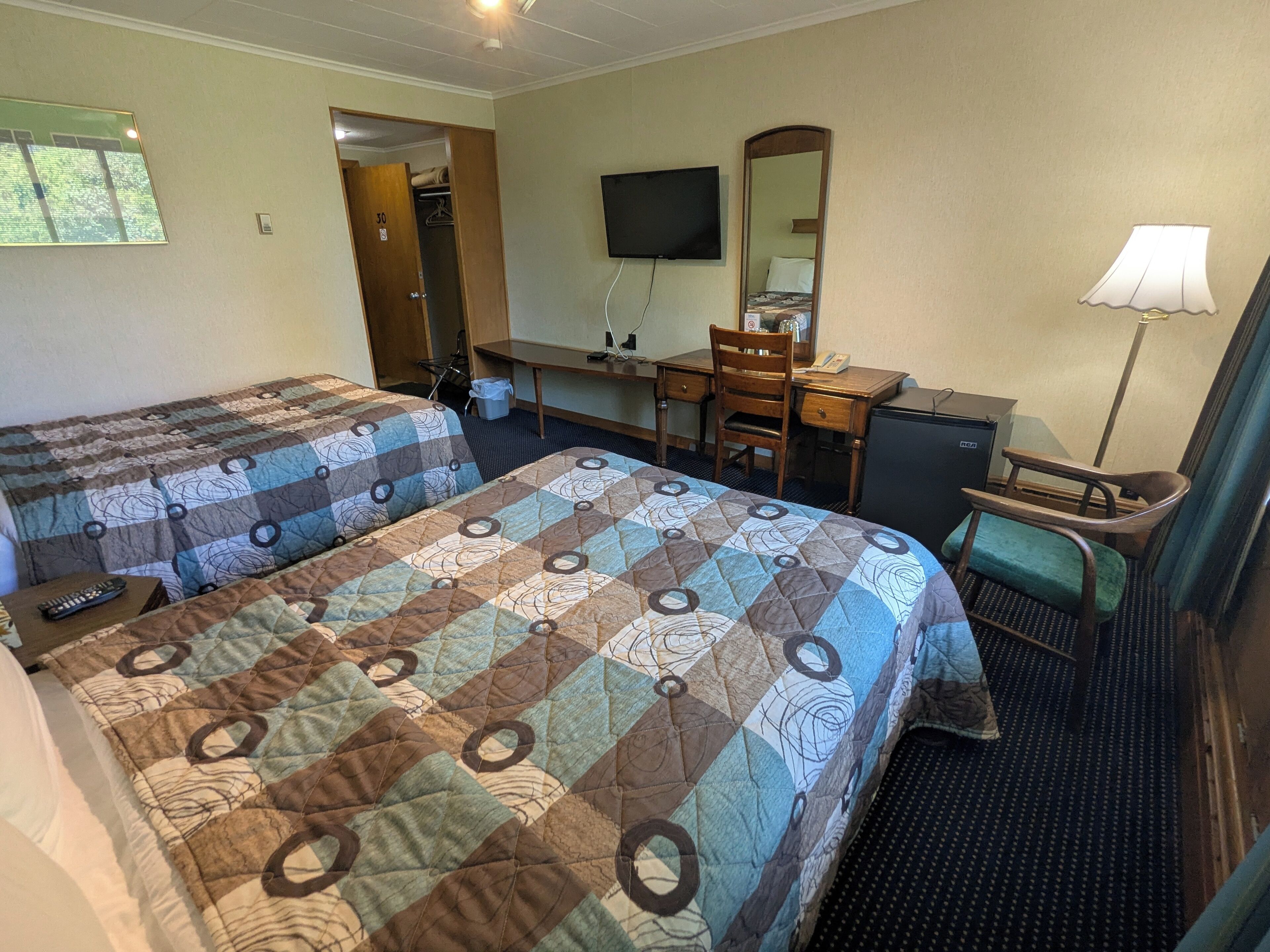 A hotel room with two beds, a desk, a chair, a TV, a mirror, and a lamp.