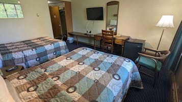 A hotel room with two beds, a desk, a chair, a TV, a mirror, and a lamp.