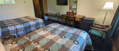 A hotel room with two beds, a desk, a chair, a TV, a mirror, and a lamp.