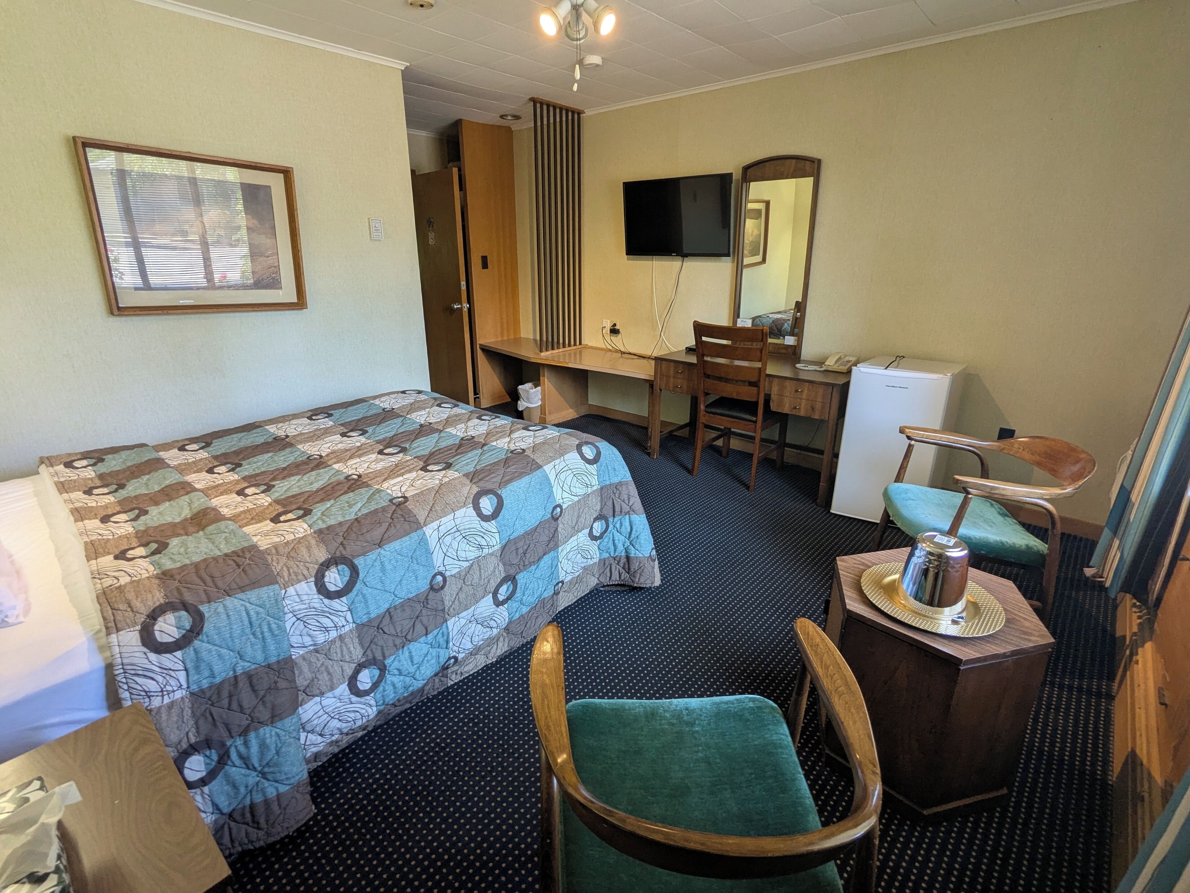 Una habitación de hotel con una cama, un escritorio, una silla, un televisor y un espejo.