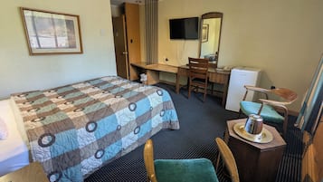 A hotel room with a bed, a desk, a chair, a television, and a mirror.