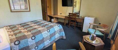 Una habitación de hotel con una cama, un escritorio, una silla, un televisor y un espejo.