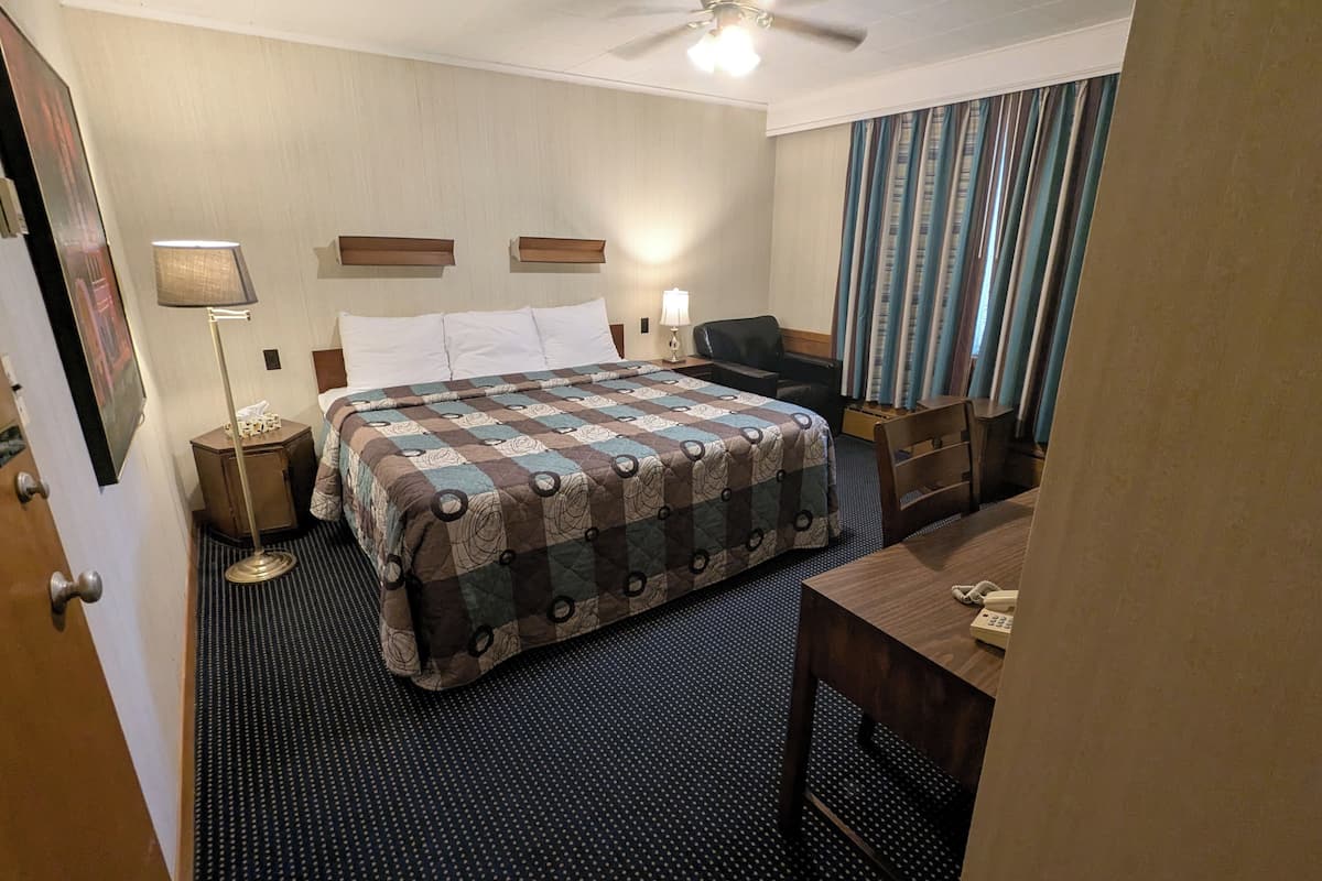 Ein Hotelzimmer mit einem großen Bett, einem Schreibtisch, einem Stuhl, einem Deckenventilator und einem Vorhangfenster.