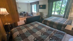 A hotel room with two beds, a desk, a chair, a lamp, and a TV.
