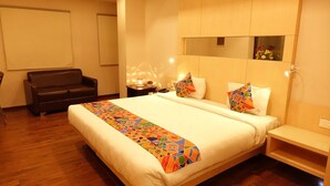 A hotel room with a large bed, a small sofa, a bedside table with a lamp, and a mirror on the wall. - Hotel K square (Chennai)