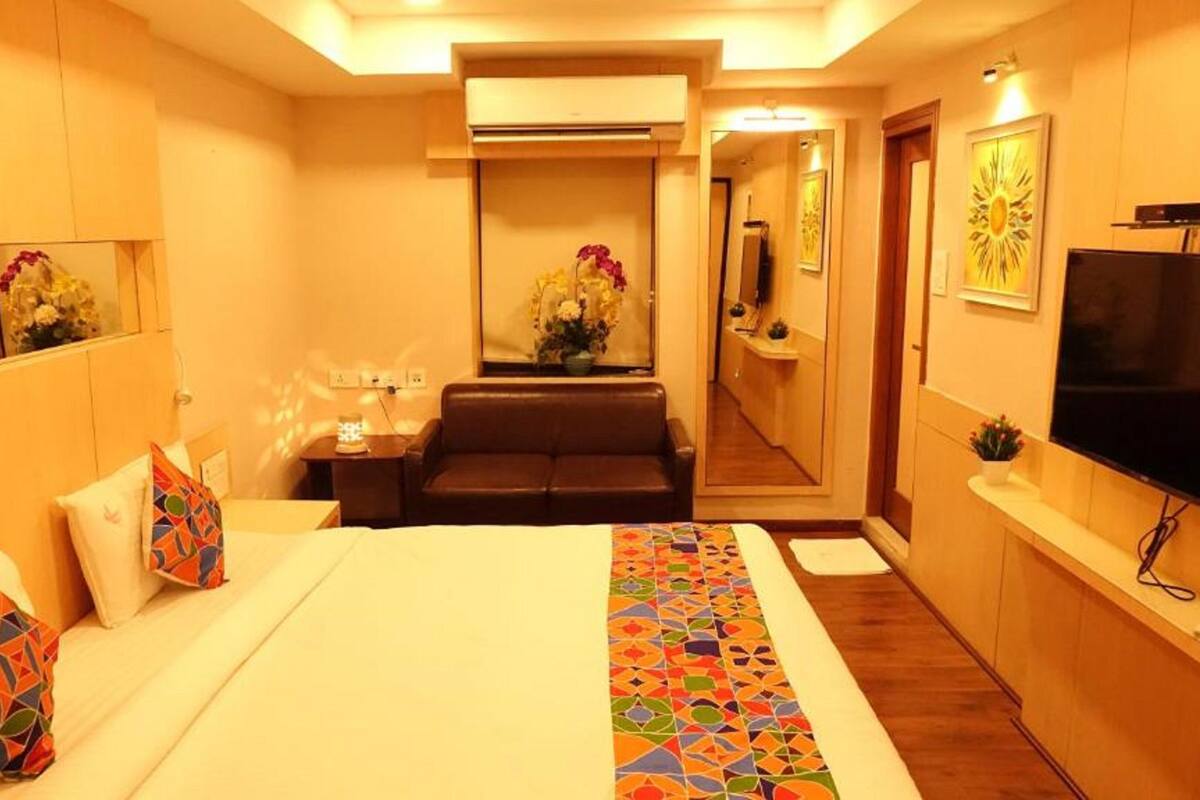 A hotel room with a bed, a sofa, a TV, and a mirror.