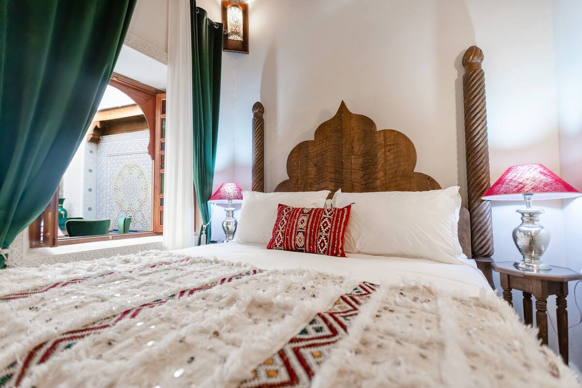 A bed with a patterned blanket, a wooden headboard, and a red pillow.