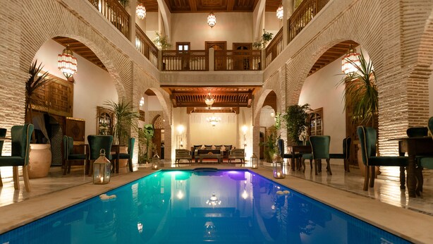 A large indoor swimming pool with a central seating area, surrounded by multiple balconies and potted plants. - Riad Janate (Marrakech)