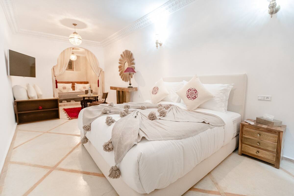 A neatly arranged bedroom with a large bed, bedside tables, a vanity, and a mirror.