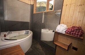 Une salle de bain avec deux baignoires séparées, une étagère en bois avec des serviettes et une vue par la fenêtre.