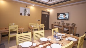 Un espace repas avec des tables et des chaises en bois, un téléviseur fixé au mur et un ventilateur de plafond.