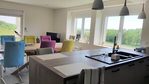 A modern kitchen with a central island, large windows, and a dining area with colorful chairs.