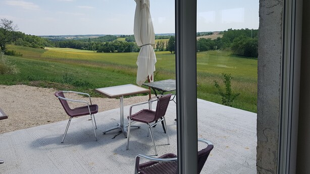 A balcony with a table and chairs, an umbrella, and a view of a green landscape.