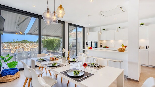 A modern dining area with a large table set for four, surrounded by white chairs. - Casa Reiet by dracmallorca (Santanyi)