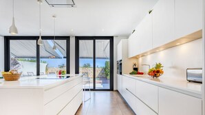 A modern kitchen with white cabinetry, a large island, and a view of the outdoors. - Casa Reiet by dracmallorca (Santanyi)