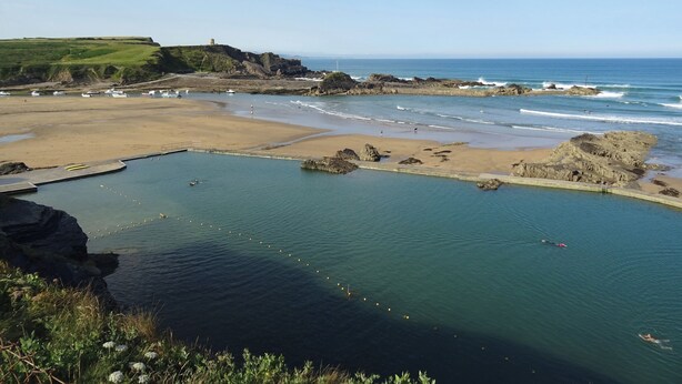 Eine Küstenlandschaft mit Strand, Felsen und ruhigem Wasser.