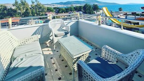 Une terrasse sur le toit, aménagée avec des meubles en osier, une piscine et une vue sur la mer et les collines lointaines.