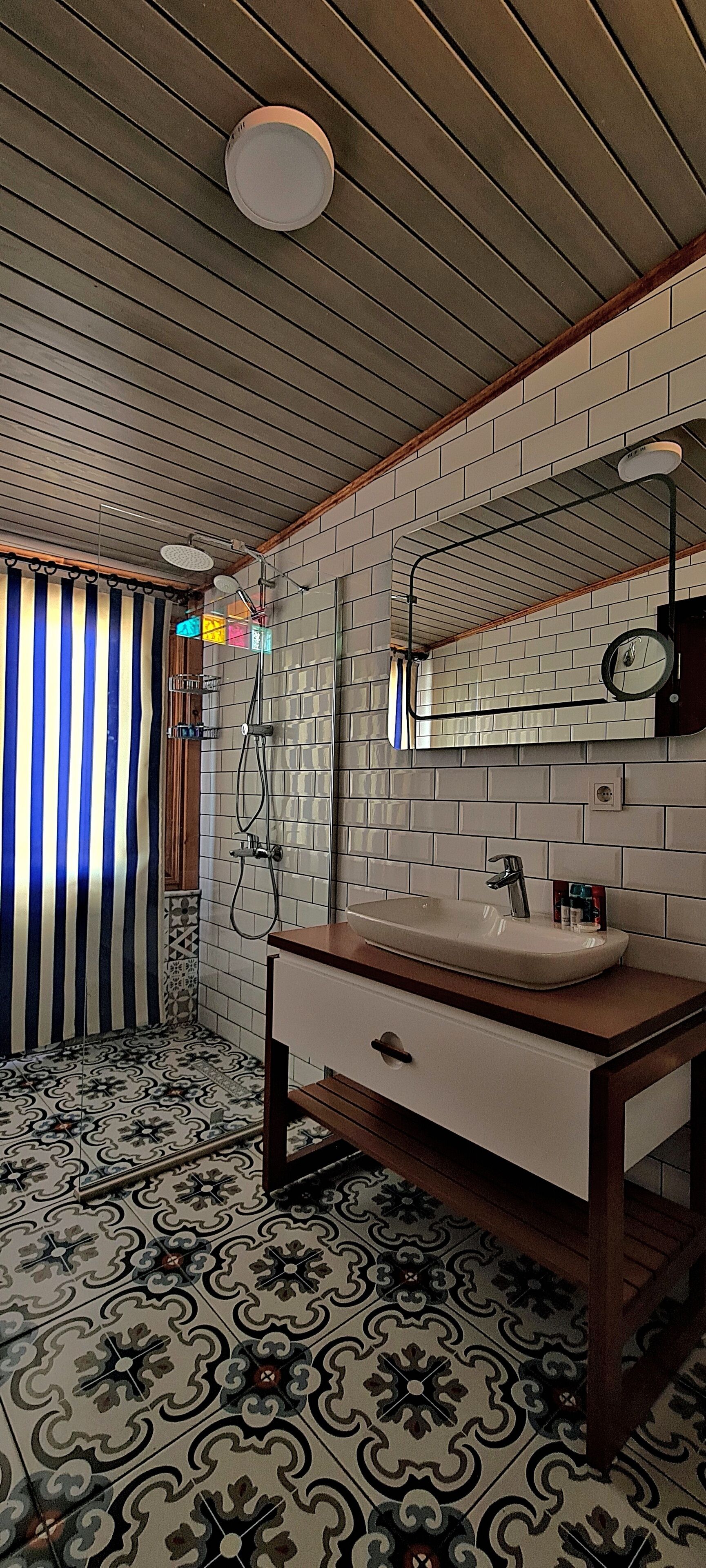 A bathroom with a tiled floor, a wooden vanity with a sink, a shower area, and a striped curtain.