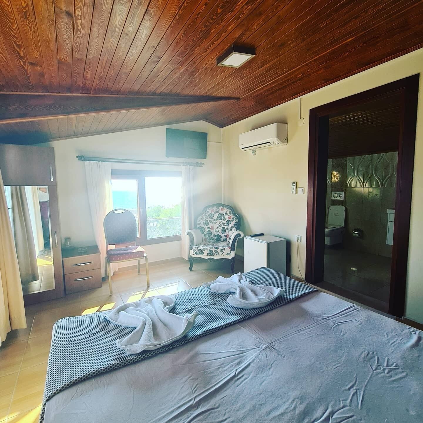 Un dormitorio con una cama, una silla, un armario pequeño y una puerta corredera que da a un baño.