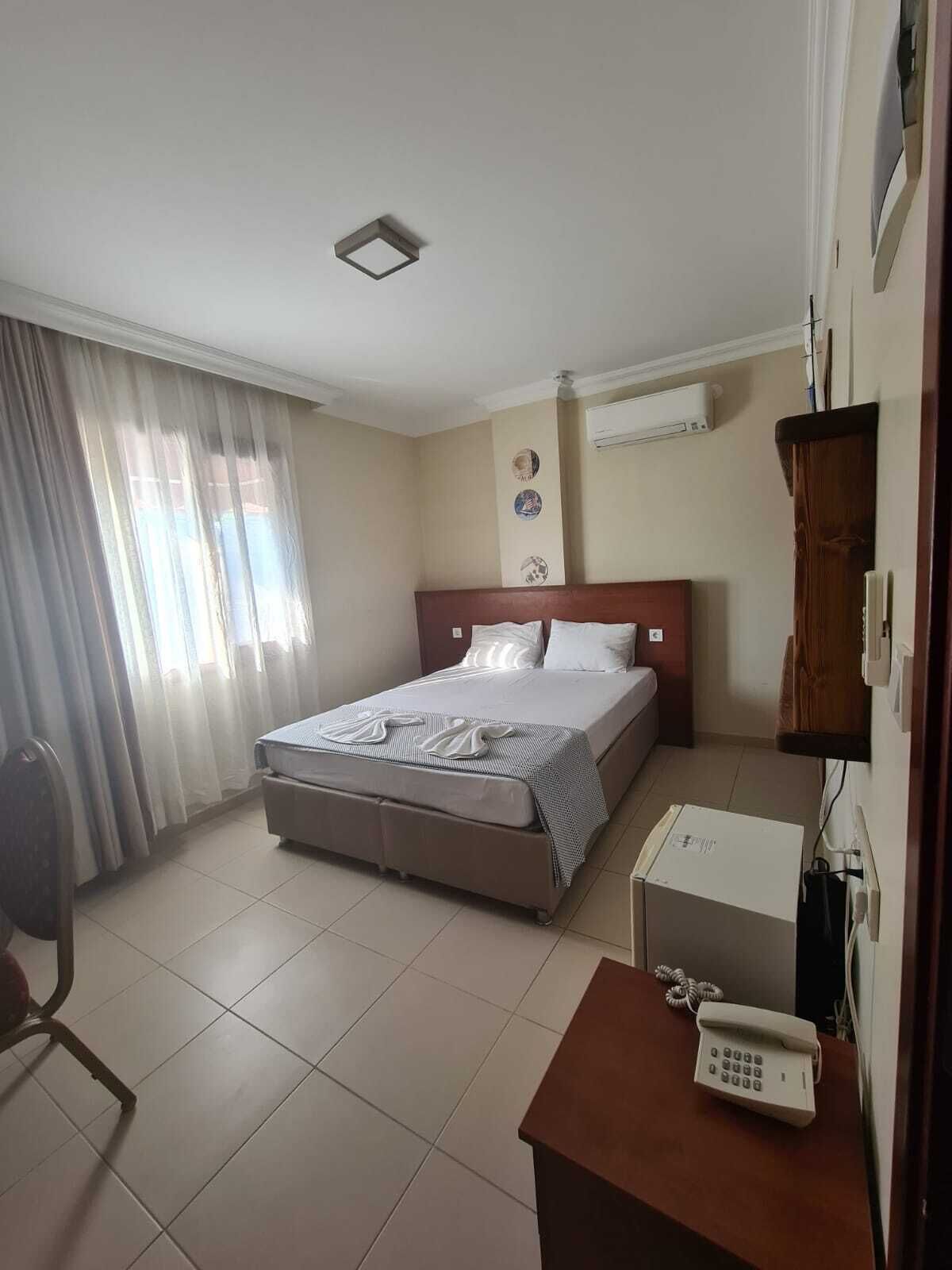 Una habitación de hotel con cama, escritorio, teléfono, silla y ventana con cortinas.