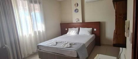 Una habitación de hotel con cama, escritorio, teléfono, silla y ventana con cortinas.