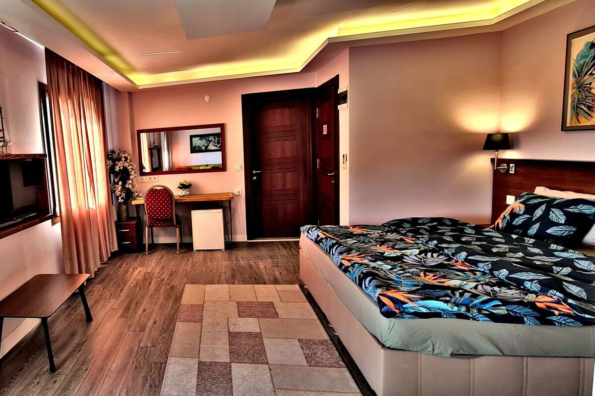 A hotel room with a bed, a desk, a chair, a TV, and a window with blinds.