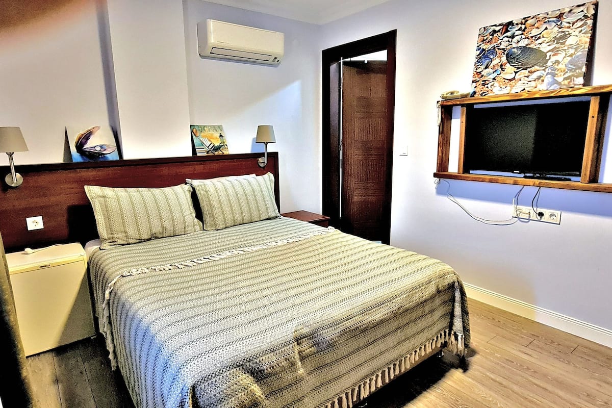 A bedroom with a bed, nightstands, a TV, and artwork on the wall.