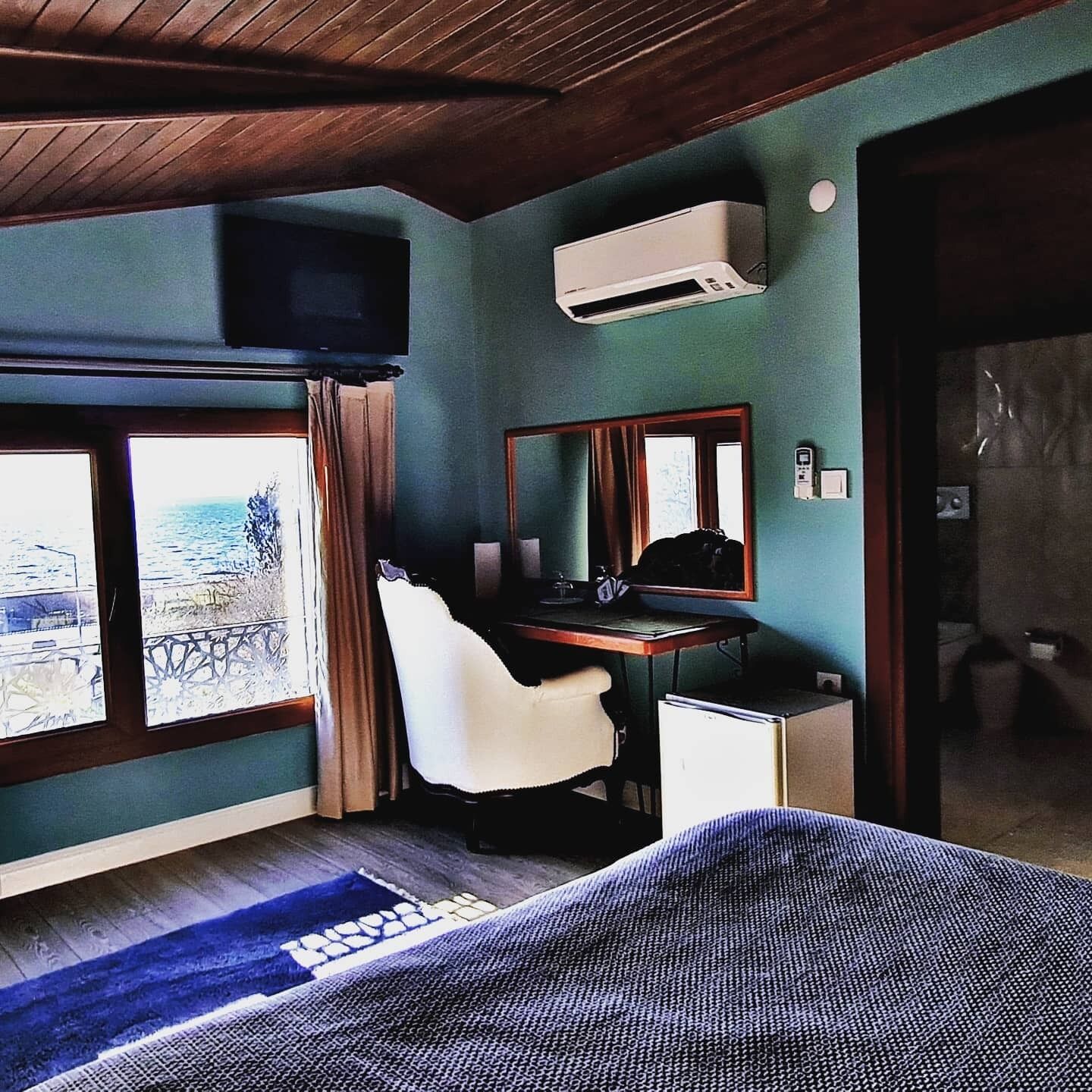A room with a bed, a desk, a chair, an air conditioner, a window with a view, and a door.