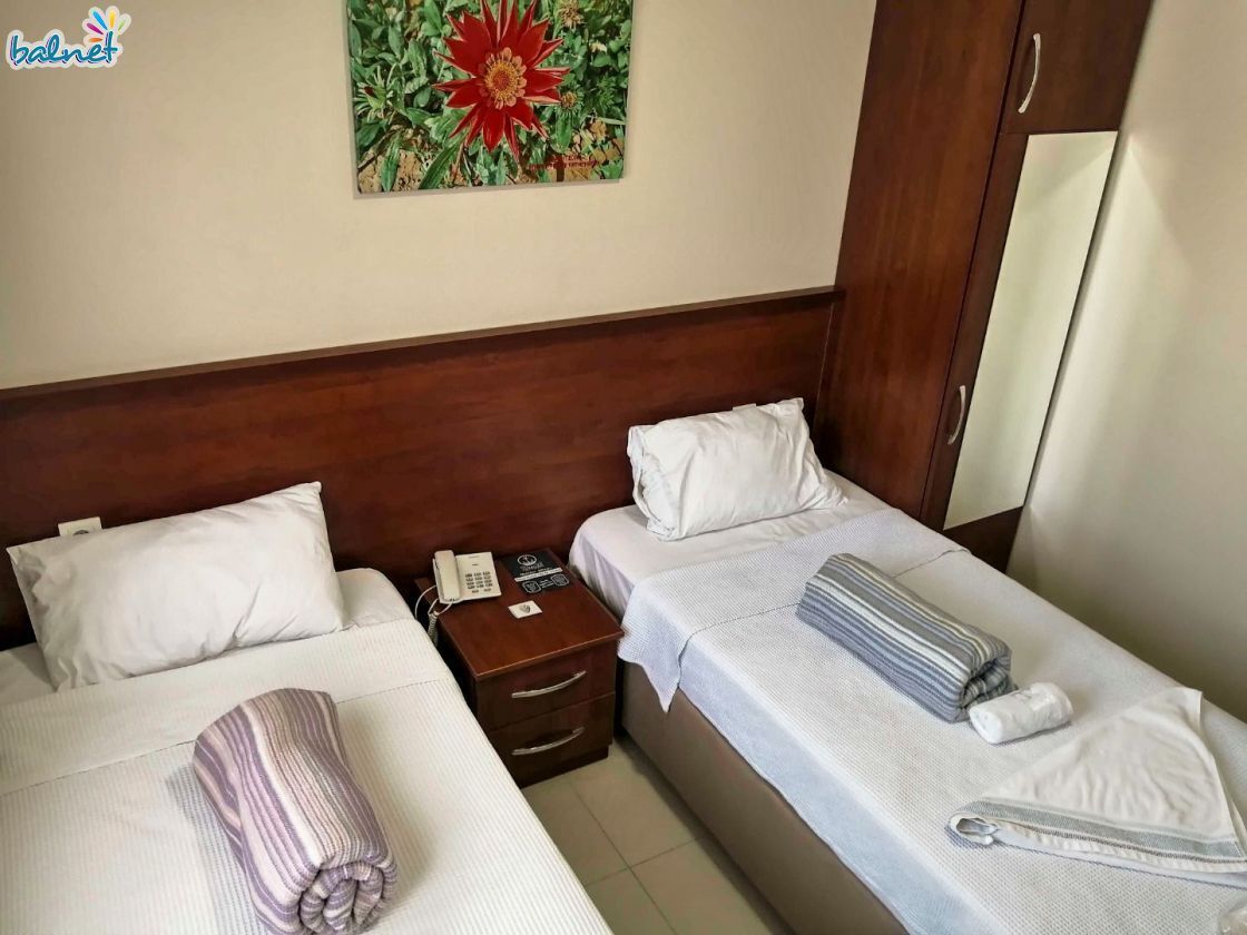 A hotel room with two beds, a wooden headboard, a bedside table with a phone, and a painting on the wall.