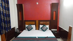 Una cama bien hecha con dos almohadas, una mesita de noche con un teléfono y una pared roja con textura.