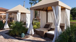 Two outdoor seating areas with canopies, surrounded by plants and a paved walkway.