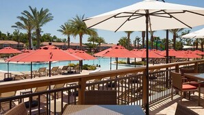 A poolside area with red umbrellas, lounge chairs, and a wooden deck.