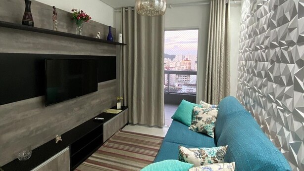 Una sala de estar moderna con un televisor de pantalla plana grande, un sofá con cojines estampados, un tapete a rayas y vistas de la ciudad por la ventana.