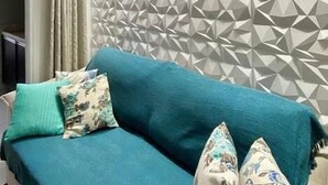Una sala de estar moderna con un sofá color turquesa, cojines estampados y un panel de pared geométrico.