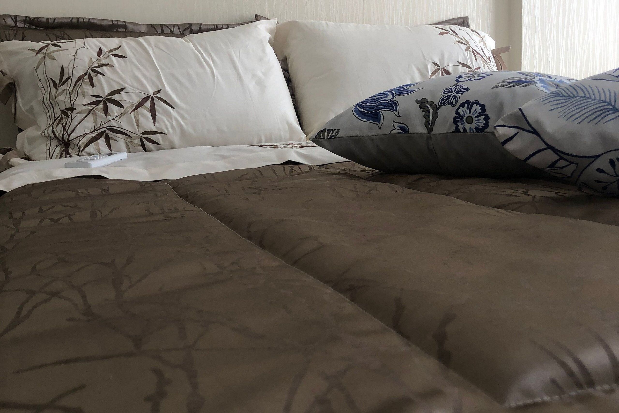 A bed with a brown patterned bedspread and decorative pillows with floral designs.