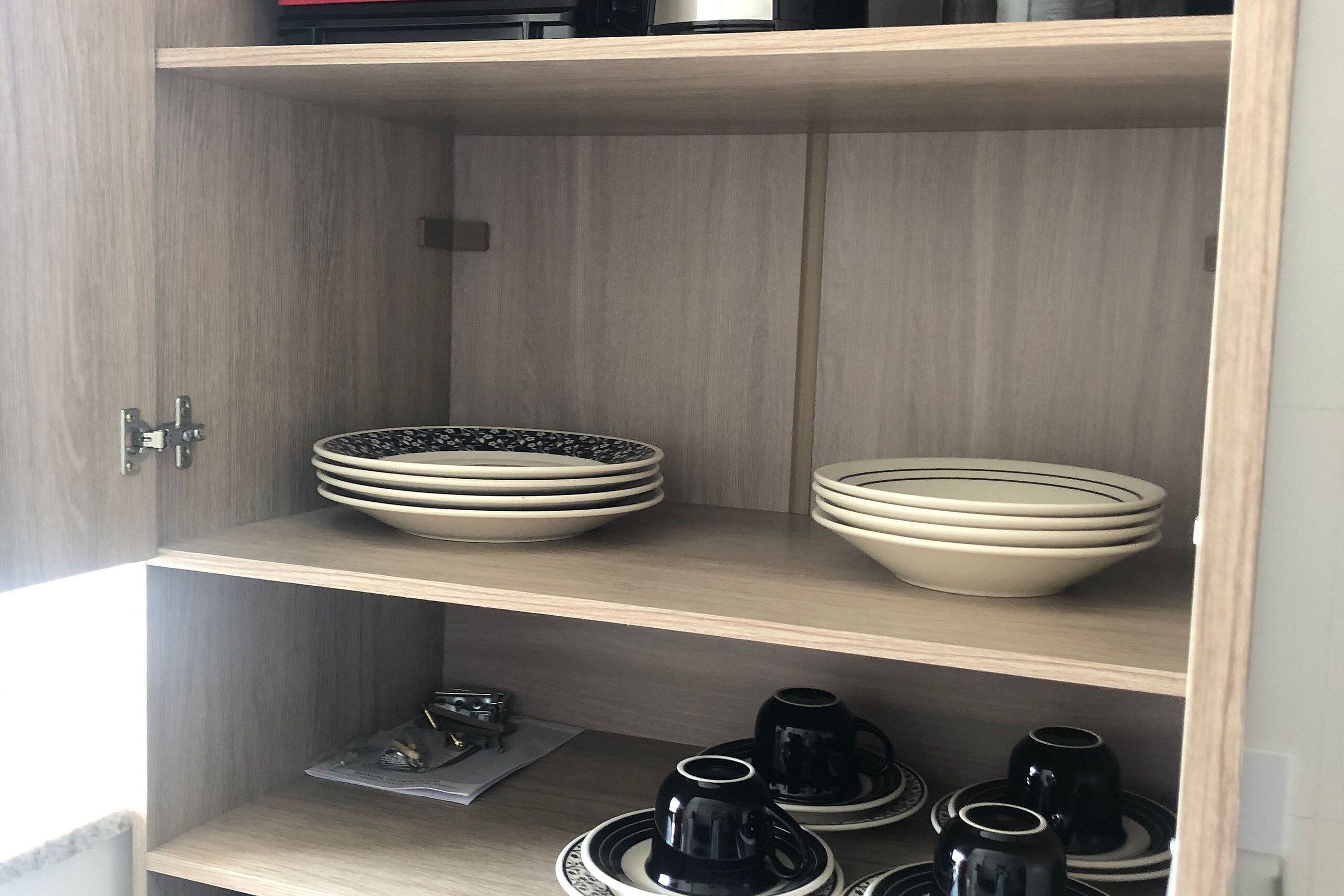 A wooden cabinet with shelves containing stacked bowls and black cups.