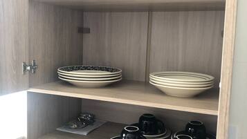 A wooden cabinet with shelves containing stacked bowls and black cups.
