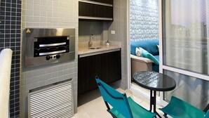 Una cocina moderna con horno empotrado, un lavamanos y armarios oscuros. Hay una pequeña mesa con dos sillas y una ventana con vistas a la ciudad.