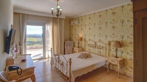 A bedroom with a large bed, a desk with a chair, a dresser, and a window with curtains.