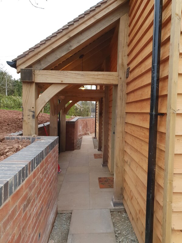 A covered outdoor area with wooden beams, brick walls, and a pathway leading to a brick building. - Lovely dog friendly cottage 4 miles from Ludlow with feature oak glass gable. (LUDLOW)