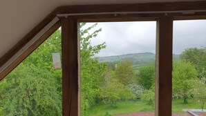 Uitzicht vanuit een kamer met houten balken en een raam dat uitkijkt over een groen landschap met bomen en een pad.