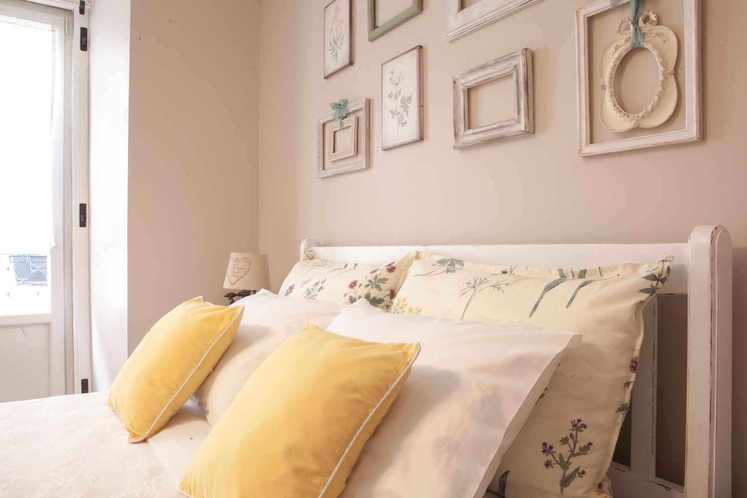 A bedroom with a bed, floral bedding, and multiple framed pictures on the wall.