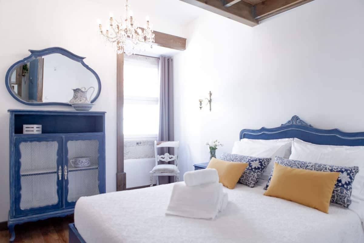 A bedroom with a bed, a dresser, a mirror, and a chandelier.
