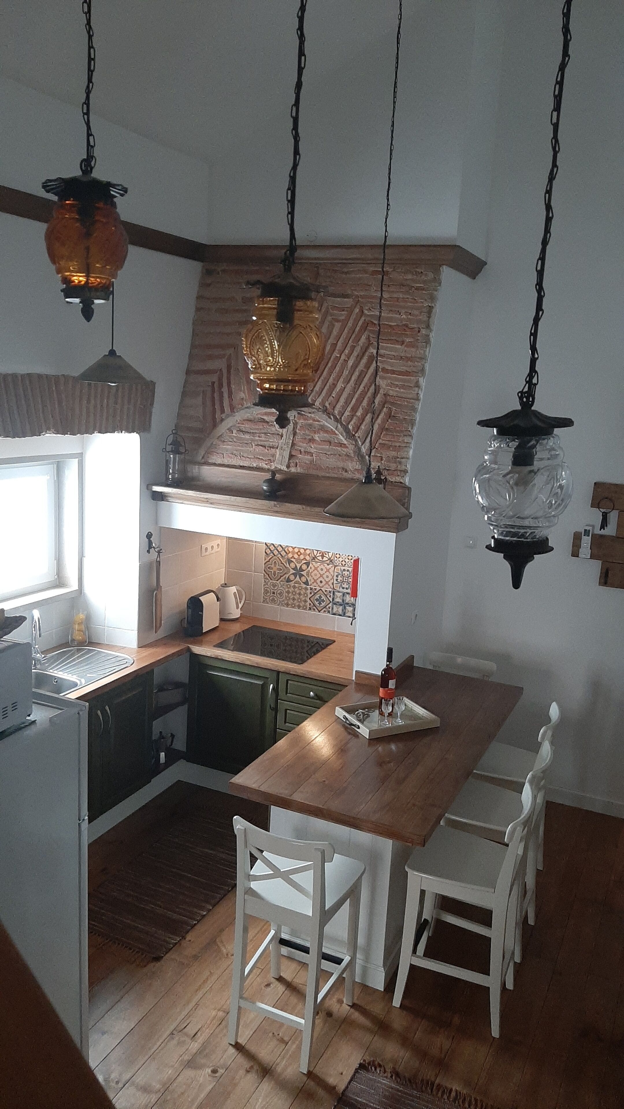 A compact kitchen with a wooden island, white chairs, and hanging pendant lights.