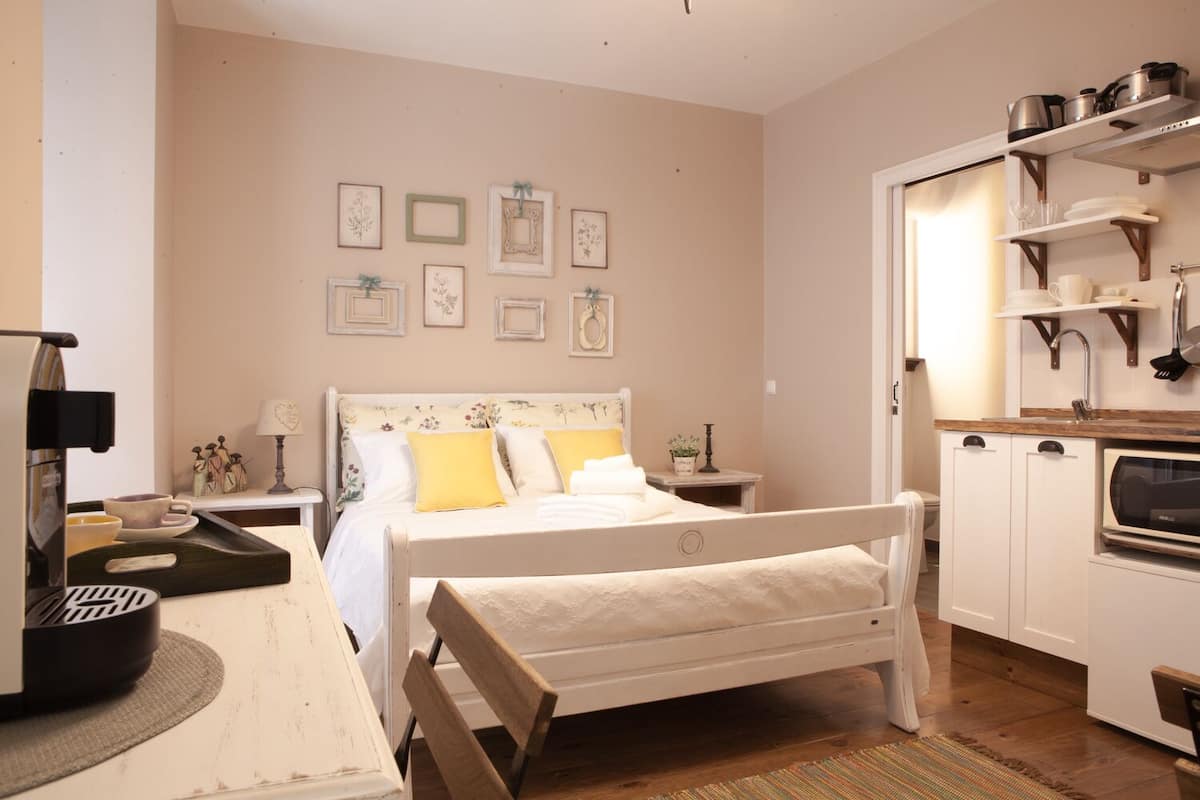 A cozy bedroom with a bed, bedside tables, a coffee machine, and a kitchenette.